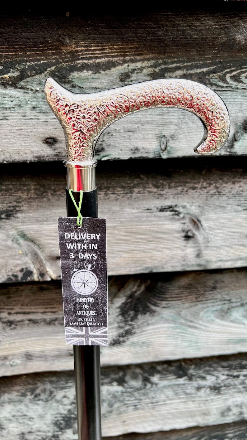 K&ouml;nnte beinhalten: Ein silberbeschlagener Gehstock mit einem verzierten Griff und einem schwarzen Holzschaft. Der Stock ist mit einem floralen Muster verziert. Ein am Stock befestigtes Schild lautet "Lieferung innerhalb von 3 Tagen" und "Ministerium f&uuml;r Antiquit&auml;ten UK-Verk&auml;ufer Versand am selben Tag".