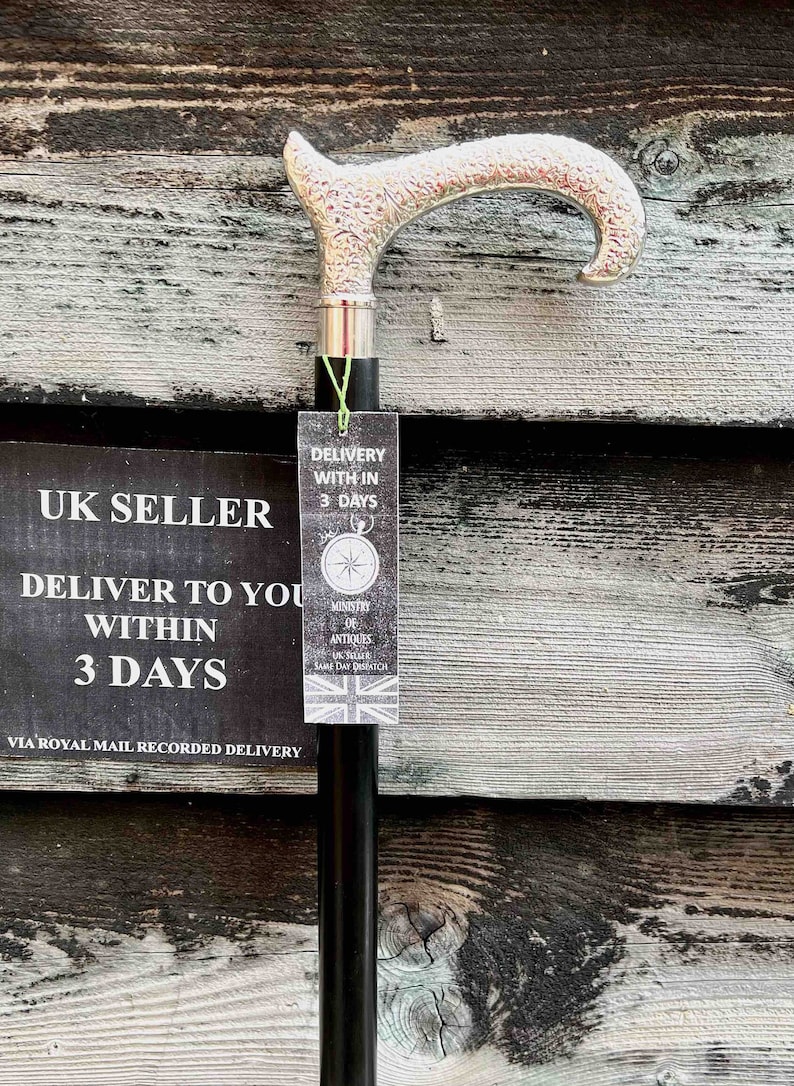K&ouml;nnte beinhalten: Ein Gehstock aus schwarzem Holz mit einem verzierten, versilberten Griff. Der Stock lehnt an einer Holzwand mit einem Schild, auf dem steht "UK Seller Deliver to you within 3 days via Royal Mail Recorded Delivery". Ein am Stock befestigtes Schild tr&auml;gt die Aufschrift "Delivery within 3 days Ministry of Antiques UK Seller Same Day Dispatch".