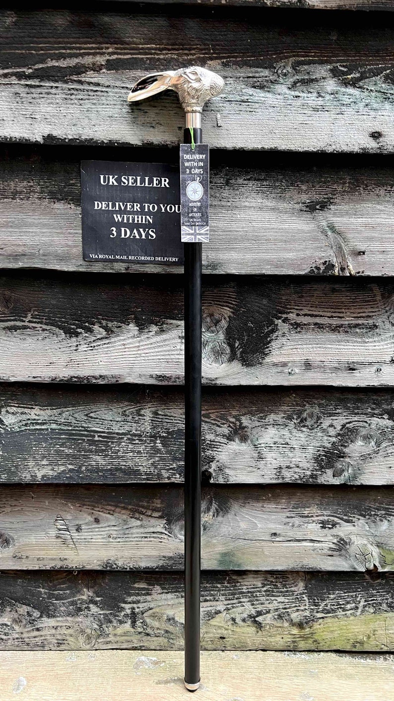 May include: A black walking stick with a silver rabbit head handle. The stick is standing upright against a wooden wall. A sign reads "UK SELLER DELIVER TO YOU WITHIN 3 DAYS VIA ROYAL MAIL RECORDED DELIVERY".