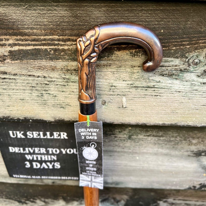 May include: A copper-colored walking stick with a detailed, ornate handle. The handle is shaped like a curved branch with a leaf design. The stick is made of wood and has a black shaft.