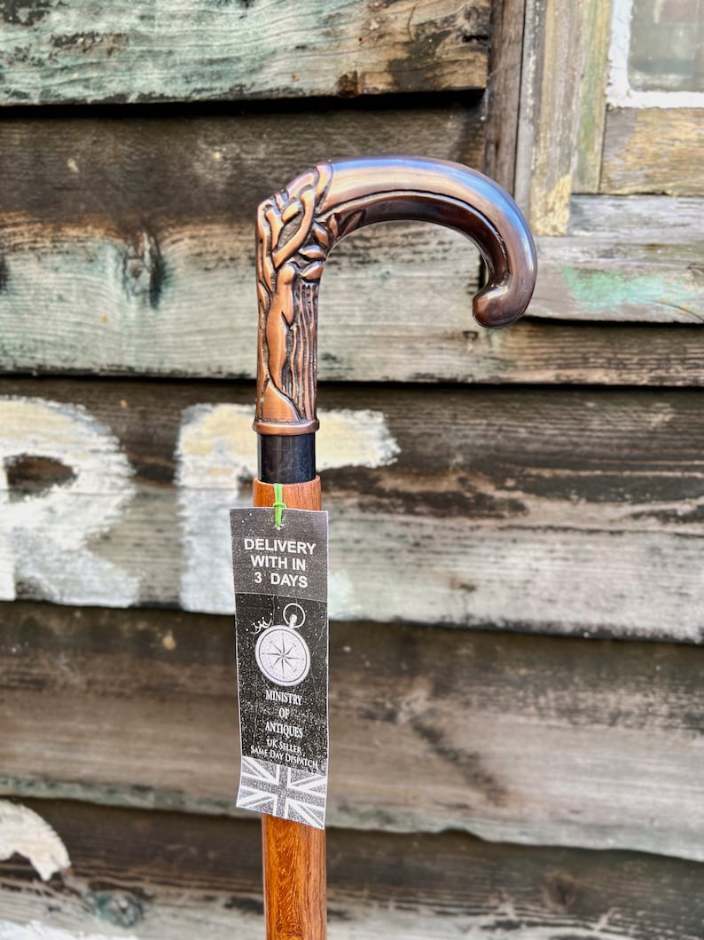 May include: A copper-colored walking stick with a detailed, ornate handle. The stick has a wooden shaft and a tag that reads "Delivery with in 3 days" and "Ministry of Antiques UK Seller Same Day Dispatch".