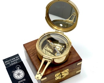 May include: A brass compass with a mirrored lid, open and revealing the compass face. The compass is sitting on a wooden box with a brass latch.