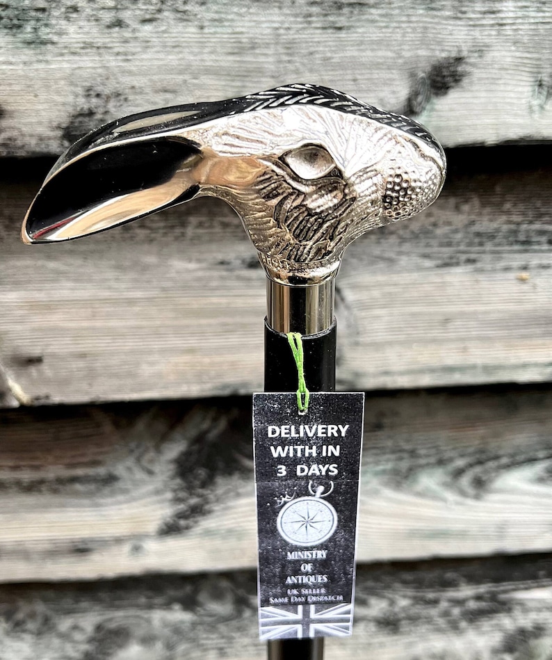 May include: A silver rabbit head walking stick with a black shaft. The stick has a tag attached that says "Delivery within 3 days" and "Ministry of Antiques".