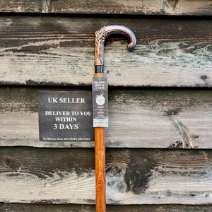 May include: A wooden walking stick with a copper-colored handle featuring a carved design. The stick is leaning against a wooden wall with a sign that reads "UK SELLER DELIVER TO YOU WITHIN 3 DAYS VIA ROYAL MAIL RECORDED DELIVERY".