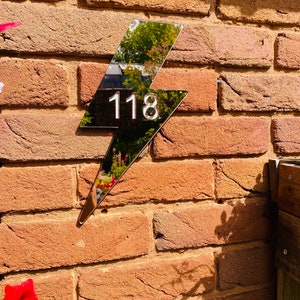 May include: A silver lightning bolt shaped house number sign with the number 118 on a brick wall.