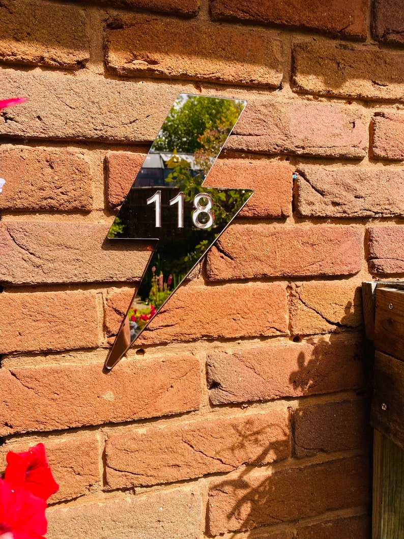 May include: A silver lightning bolt shaped house number sign with the number 118 on a brick wall.