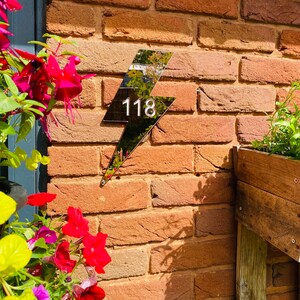 May include: Black lightning bolt shaped house number sign with the number 118 on a brick wall.