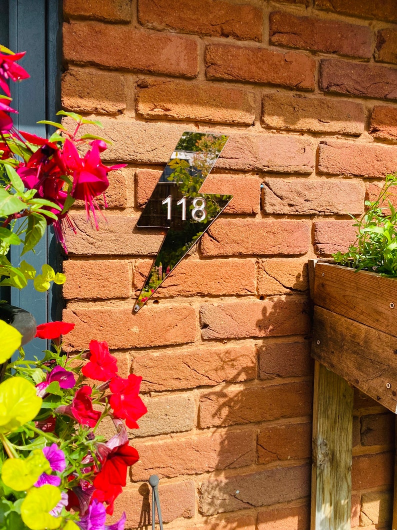 May include: Black lightning bolt shaped house number sign with the number 118 on a brick wall.