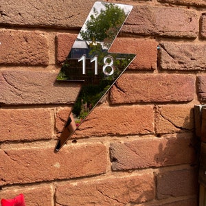 May include: A silver lightning bolt shaped house number sign with the number 118 on it. The sign is mounted on a brick wall.