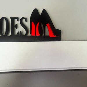 May include: Black wooden sign with the word "Shoes" and two black high heel shoes with red soles.