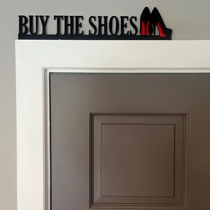 May include: Black wooden sign with the text "BUY THE SHOES" and a pair of red high heels.