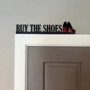 May include: Black metal sign with the text "BUY THE SHOES" and a pair of red high heels.