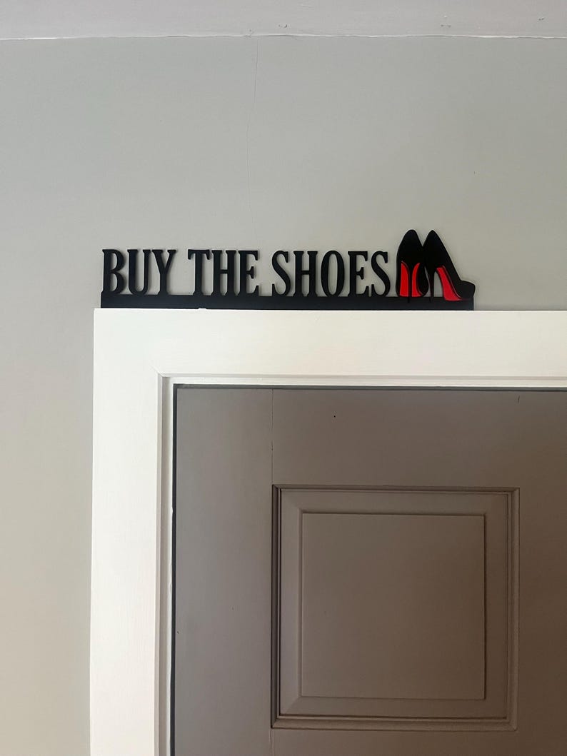 May include: Black metal sign with the text "BUY THE SHOES" and a pair of red high heels.