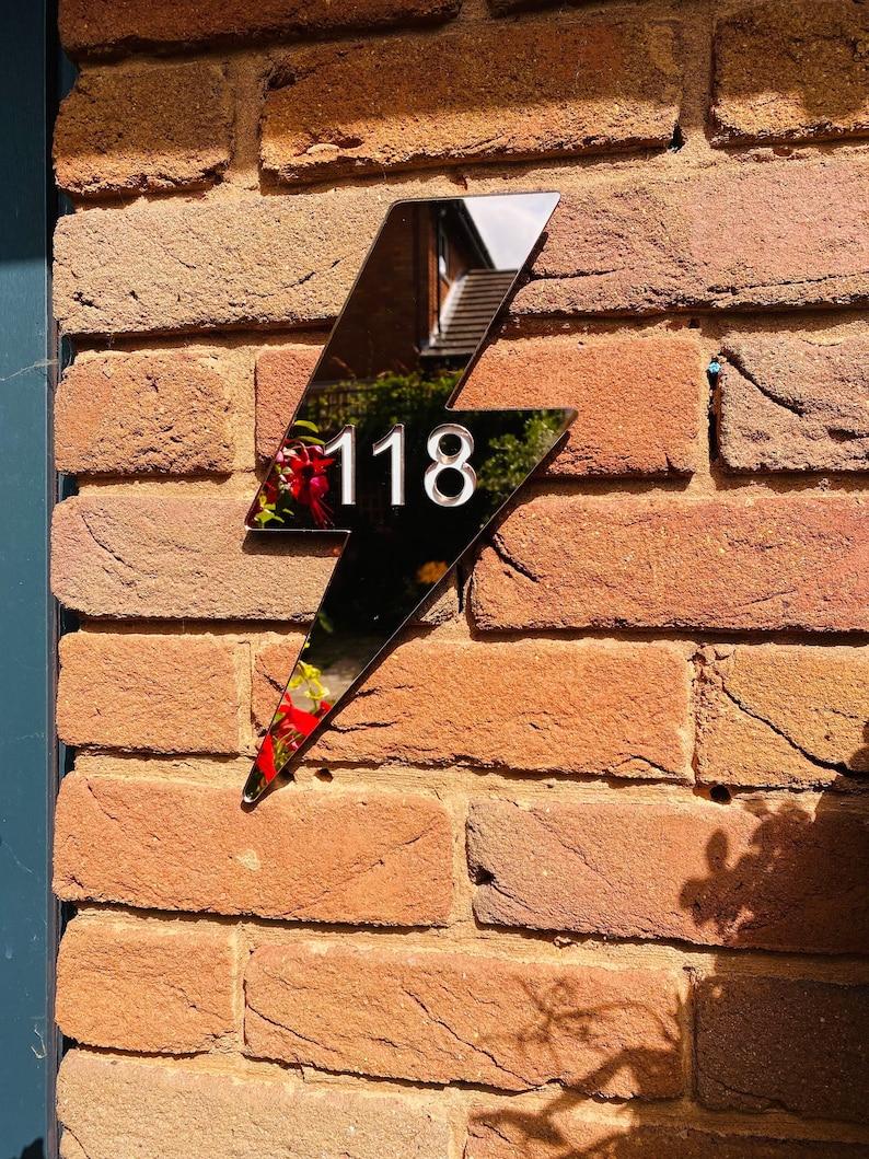 May include: A black lightning bolt shaped house number sign with the number 118 in white on a brick wall.