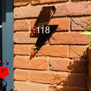 May include: A black lightning bolt shaped house number sign with the number 118 in white on a brick wall.