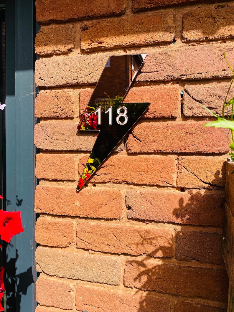 May include: A black lightning bolt shaped house number sign with the number 118 in white on a brick wall.