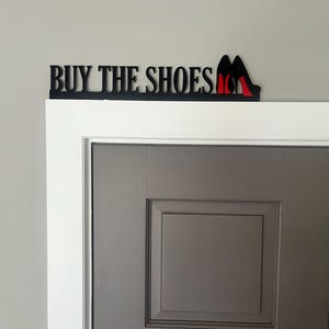 May include: Black metal sign with the text "BUY THE SHOES" and a pair of red high heels.