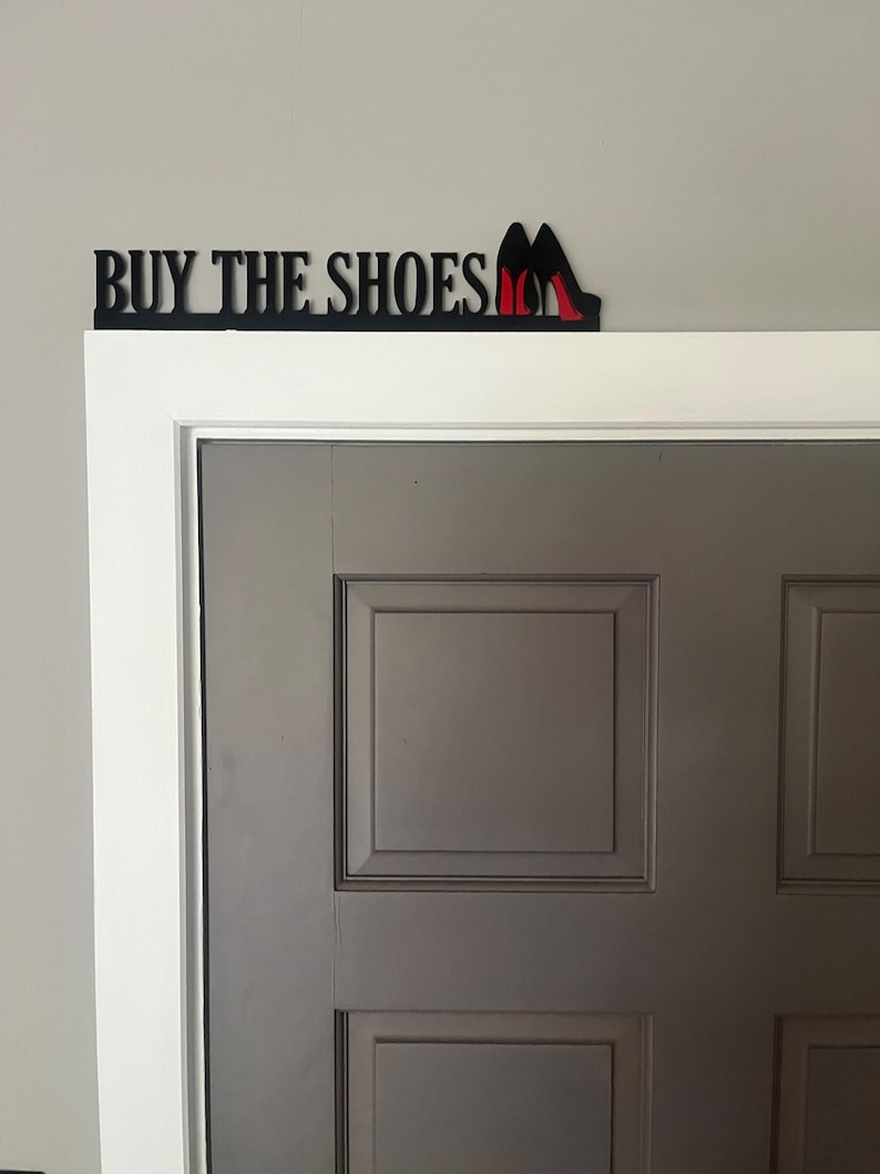 May include: Black metal sign with the words "BUY THE SHOES" and a pair of red high heels.