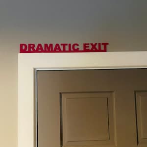 Puede incluir: Una puerta blanca con un letrero rojo encima que dice "Salida Dram&aacute;tica".