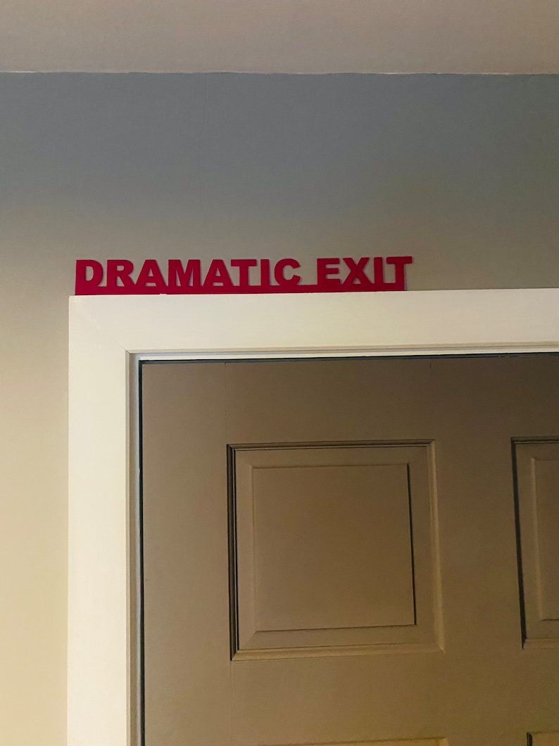 Puede incluir: Una puerta blanca con un letrero rojo encima que dice "Salida Dram&aacute;tica".