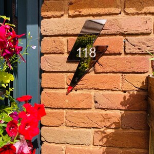 May include: Black lightning bolt shaped house number sign with the number 118 in white on a brick wall.