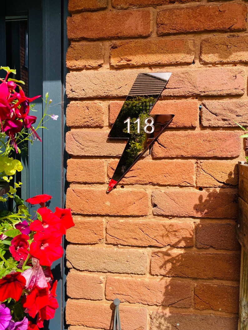May include: Black lightning bolt shaped house number sign with the number 118 in white on a brick wall.