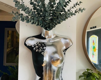May include: A silver and black painted mannequin torso with a leafy green plant growing out of the top of its head.