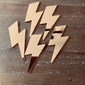 May include: Five gold mirror lightning bolt shapes arranged in a cluster on a wooden background.