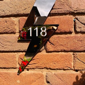 May include: A black lightning bolt shaped house number sign with the number 118 in white on a brick wall.