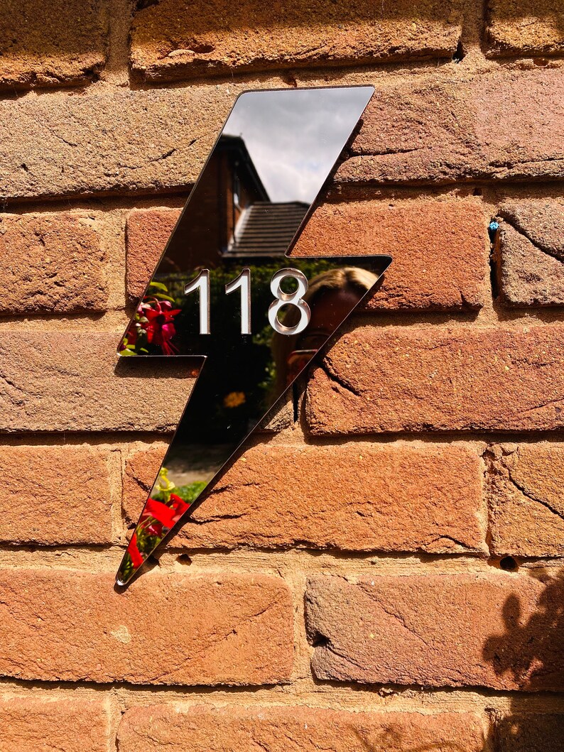 May include: A black lightning bolt shaped house number sign with the number 118 in white on a brick wall.
