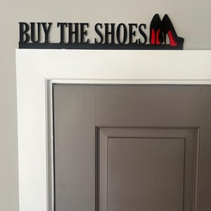 May include: Black wooden sign with the text "BUY THE SHOES" and two red high heel shoes.