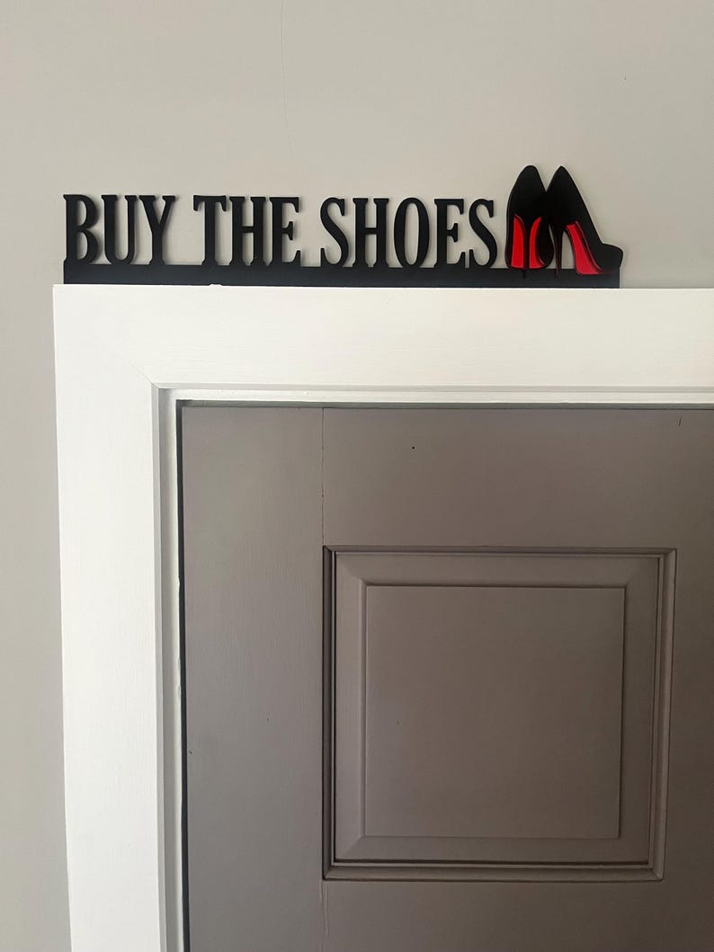 May include: Black wooden sign with the text "BUY THE SHOES" and two red high heel shoes.