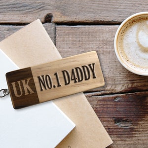 May include: A wooden keyring with the text "UK NO.1 DADDY" engraved on it. The keyring is brown and has a silver metal ring.
