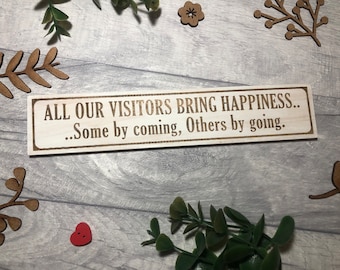 Op de afbeelding: Houten bord met de tekst "ALL OUR VISITORS BRING HAPPINESS... Some by coming, Others by going."