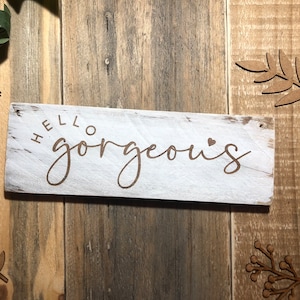 May include: White wooden sign with the text "HELLO gorgeous" in brown lettering with a small heart symbol.