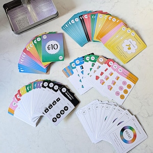 May include: A board game with a variety of cards, including property wild cards and activity cards. The cards display values in Euros and instructions. A metal tin with instructions is visible. The game is designed for multiple players.