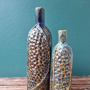 May include: Two ceramic vases with a textured, honeycomb-like design. The larger vase is blue and brown, while the smaller vase is green and brown.