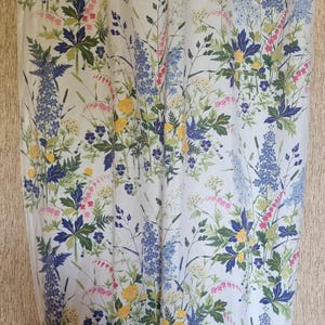 May include: A white fabric with a floral pattern featuring blue, yellow, green, and pink flowers. The fabric has a subtle texture and a light, airy feel.