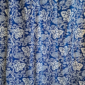 May include: Close-up of a blue fabric with a white grape and leaf pattern. The design features clusters of grapes, leaves, and vines, creating a repeating floral motif. The fabric has a textured appearance.
