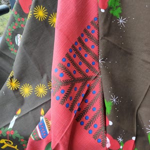 Op de afbeelding: Close-up van drie gevouwen stoffen met kerstthema. Eén is rood met een diagonaal patroon en blauwe stippen, een andere is bruin met gele sterren en kaarsen, en de derde is bruin met kerstmanfiguren en sneeuwvlokken.