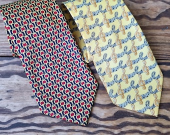 Può includere: Due cravatte fantasia. Una presenta un motivo ripetuto di cerchi rossi all'interno di un design blu navy e oro. L'altra è gialla con un motivo ripetuto di note musicali e chiavi di violino in blu e oro.