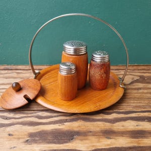Könnte beinhalten: Ein Satz aus drei Salz- und Pfefferstreuern aus Holz mit Metalldeckeln, auf einem Holztablett mit einem Metallgriff. Das Tablett hat einen Deckel mit einem Holzgriff.