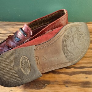 May include: Close-up of the bottom of a burgundy leather loafer with a brown sole. The sole has the text "Elastiche" and "Made in Italy" printed on it. The size 41 is also visible.
