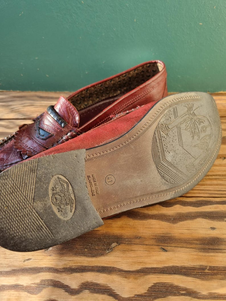 May include: Close-up of the bottom of a burgundy leather loafer with a brown sole. The sole has the text "Elastiche" and "Made in Italy" printed on it. The size 41 is also visible.