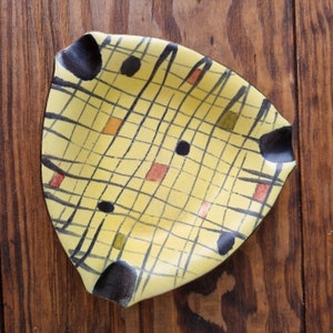 Peut inclure: Un plat en céramique jaune avec un motif géométrique noir et brun. Le plat a un motif de grille avec des lignes noires et des accents bruns. Le plat est parfait pour servir des collations ou des amuse-gueules.