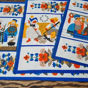 Puede incluir: Juego de tres manteles individuales blancos con borde azul e ilustraciones de arte popular. Cada mantel individual presenta una escena diferente de personas con vestimenta tradicional, con patrones florales y de hojas en naranja, azul y marrón.