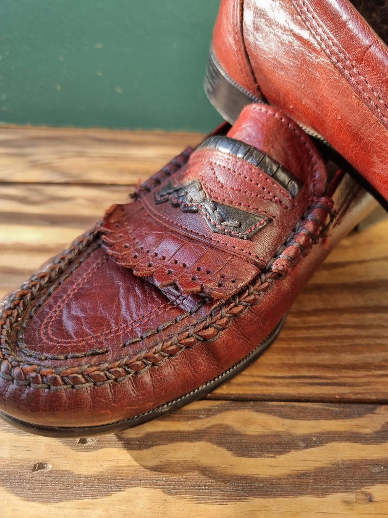 May include: A pair of brown leather loafers with a braided trim and a decorative stitch pattern. The loafers have a pointed toe and a low heel.