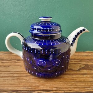 Op de afbeelding: Een blauwe en witte theepot van keramiek met een geometrisch patroon. De theepot heeft een rond lichaam en een deksel met een knop bovenop. De tuit bevindt zich aan de zijkant van de theepot en de handgreep aan de andere kant.
