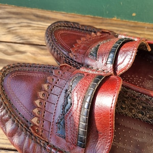 May include: A pair of brown leather loafers with black stitching and a decorative design. The loafers have a closed toe and a slip-on style.