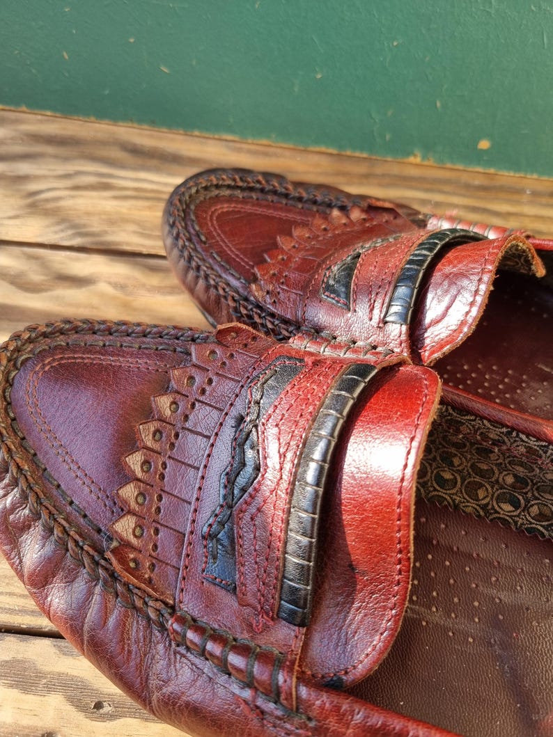 May include: A pair of brown leather loafers with black stitching and a decorative design. The loafers have a closed toe and a slip-on style.